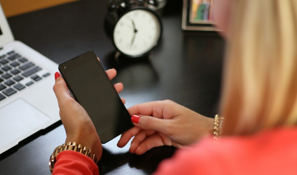 woman sitting holding smartphone near laptop